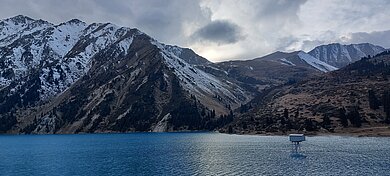 Berglandschaft mit schneebedeckten Gipfeln und einem See im Vordergrund unter bewölktem Himmel