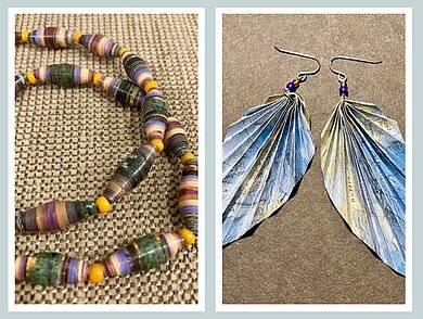 Das Bild zeigt handgefertigten Schmuck aus Papier: links eine bunte Kette aus aufgerollten Papierperlen, rechts ein Paar gefaltete Ohrringe in blauen und beigen Farbtönen.