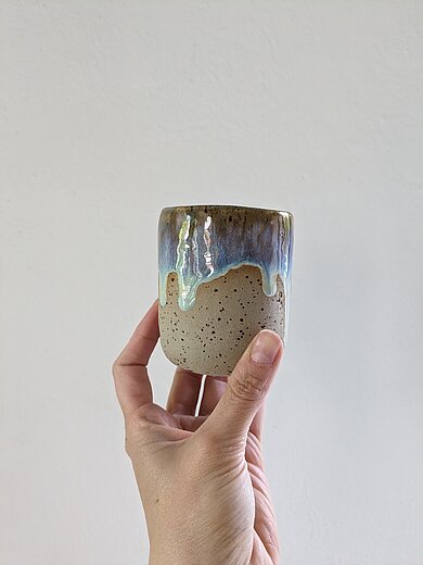 Bild einer Hand, die einen getöpferten Becher mit Glasur hält.
